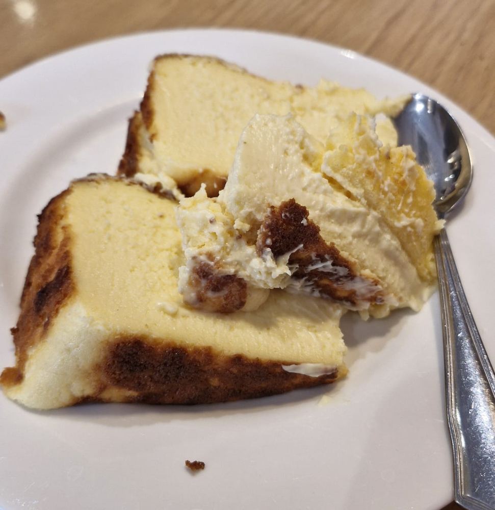 Two slices of burnt Basque cheesecake on a white plate with a spoon
