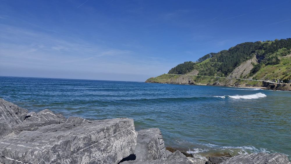 Deep blue sea, grey rocks and a green cliff along the Basque coast under a clear sky